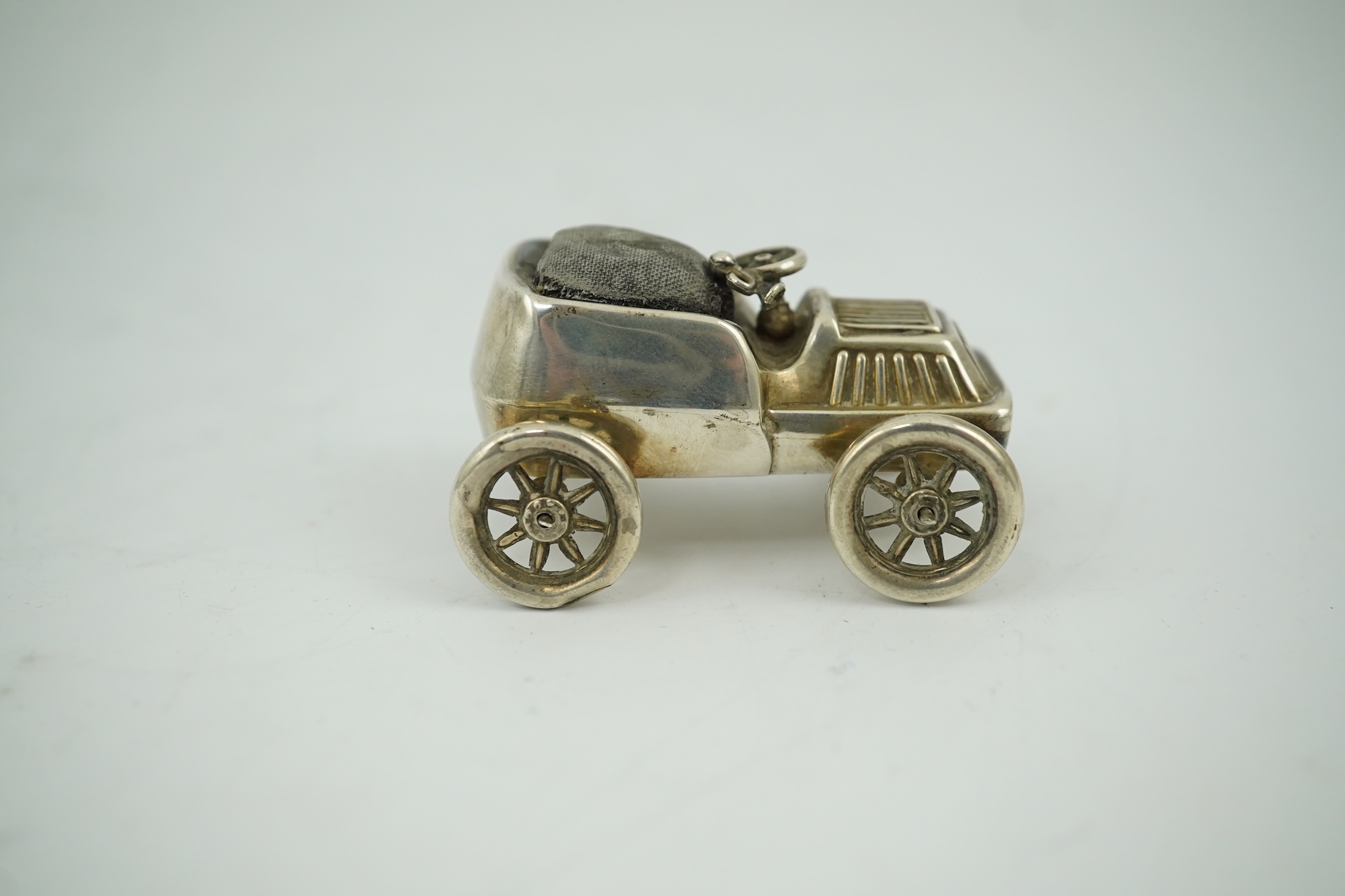 An Edwardian novelty silver mounted pin cushion modelled as a vintage car, makers mark rubbed, Birmingham, 1906, 57mm. Condition - poor to fair